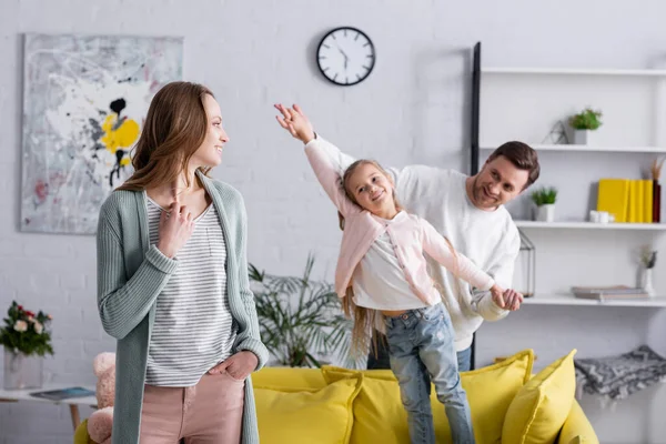 Frau lächelt, während sie Mann und Tochter auf verschwommenem Hintergrund an den Händen hält — Stockfoto