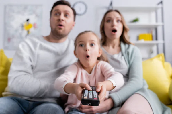 Remote controller in hands of excited kid near parents on blurred background — Stock Photo