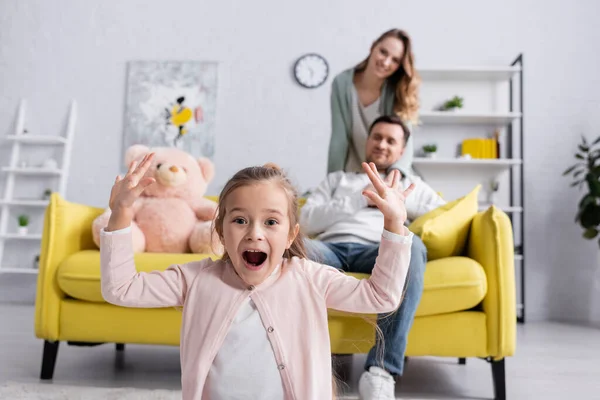 Enfant excité regardant la caméra près des parents sur fond flou — Photo de stock