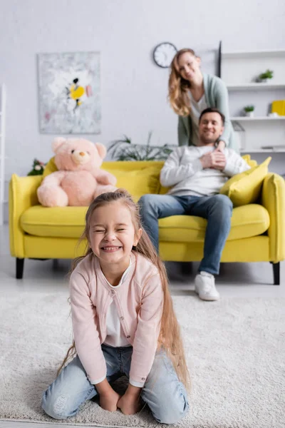 Glückliches Mädchen sitzt neben Eltern auf verschwommenem Hintergrund im Wohnzimmer — Stockfoto