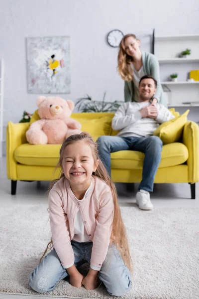 Fille heureuse assise près des parents sur fond flou dans le salon — Photo de stock