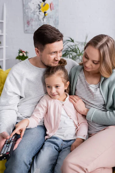 Padres sentados cerca de hija con mando a distancia - foto de stock