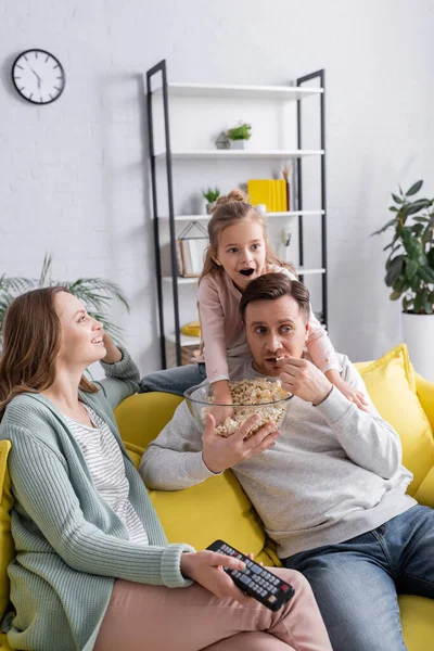 Hombre sosteniendo palomitas de maíz cerca de hija y esposa con controlador remoto - foto de stock