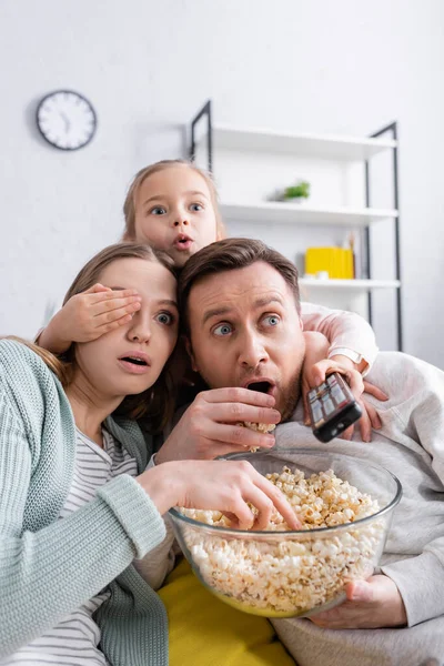 Emocionado niño sosteniendo mando a distancia cerca de los padres con palomitas de maíz - foto de stock