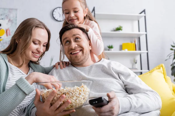Positive kid looking at parents with popcorn and remote controller — Stock Photo