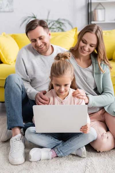 Ребенок с помощью ноутбука рядом улыбающихся родителей на размытом фоне дома — стоковое фото