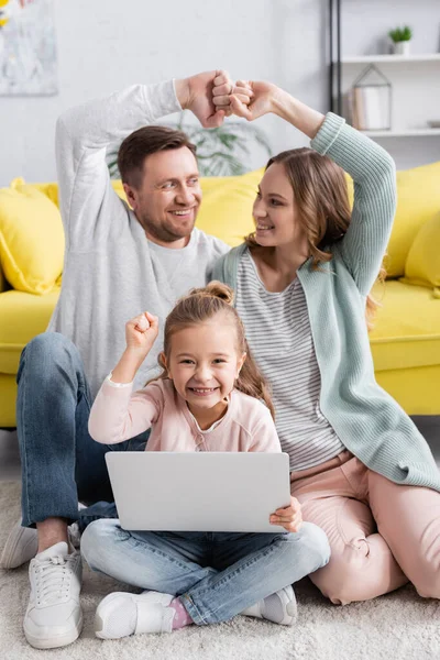 Girl with laptop showing yes gesture near smiling parents on blurred background — Stock Photo