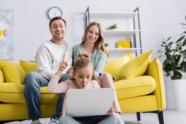 Excited kid having idea while using laptop near parents on blurred background — Stock Photo