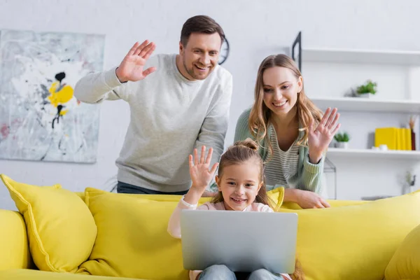 Smiling kid having video call on laptop near parents on blurred background — Stock Photo