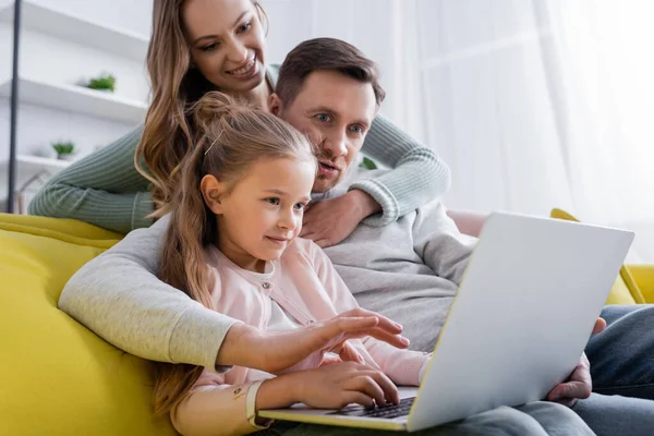 Человек, использующий ноутбук с дочерью рядом улыбающаяся жена на размытом фоне — стоковое фото
