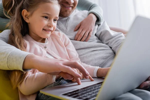 Bambino sorridente che utilizza il computer portatile vicino ai genitori su sfondo sfocato — Foto stock