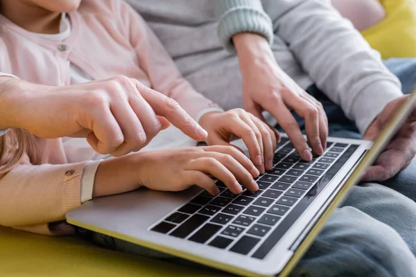 Cropped view of man pointing with finger while using laptop with daughter and wife — Stock Photo