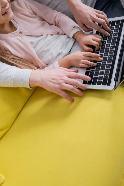 Vue recadrée d'un enfant souriant utilisant un ordinateur portable près des parents sur un canapé jaune — Photo de stock
