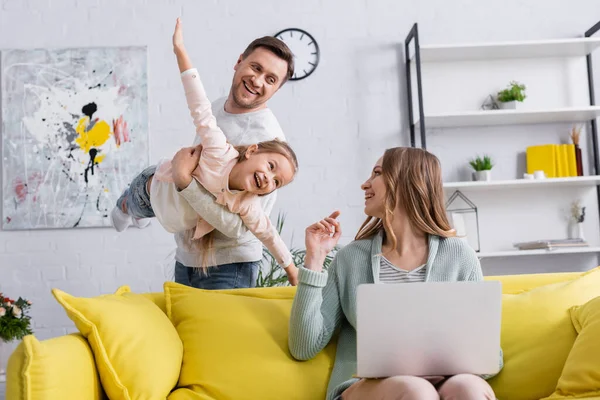 Sorridente madre con computer portatile guardando la famiglia divertirsi a casa — Foto stock