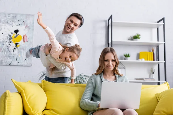 Freelancer using laptop near cheerful husband and kid having fun — Stock Photo