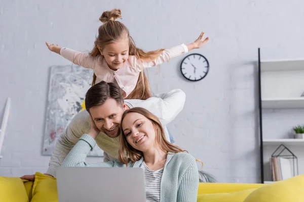 Donna sorridente utilizzando laptop vicino al marito e al bambino a casa — Foto stock