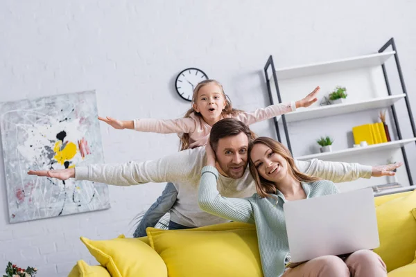 El hombre y la hija se divierten cerca de la esposa sonriente utilizando el ordenador portátil en casa - foto de stock