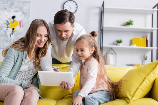 Mann benutzt digitales Tablet neben lächelnder Frau und Tochter auf Couch — Stockfoto