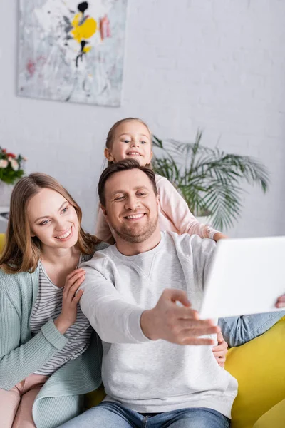 Smiling family with child taking selfie on digital tablet on blurred foreground — Stock Photo