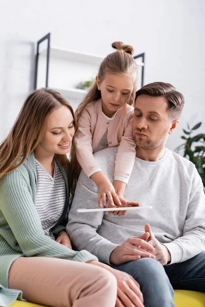 Kid using digital tablet near parents on couch — Stock Photo