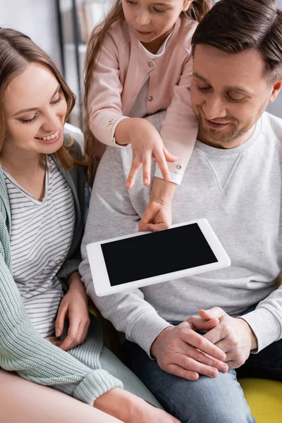 Tableta digital con pantalla en blanco en la mano del niño cerca de padres sonrientes en casa - foto de stock