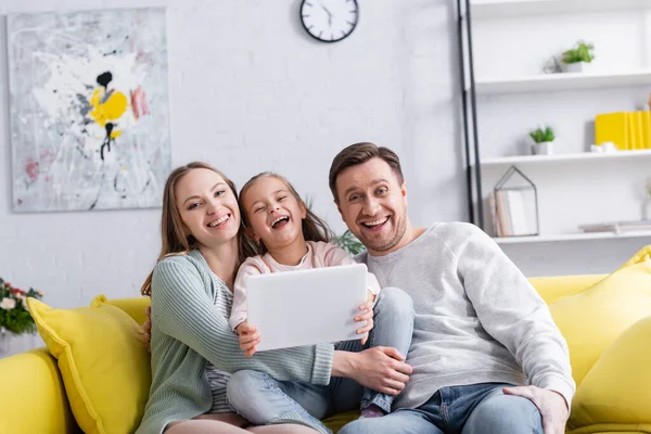 Femme positive étreignant fille avec tablette numérique près du mari — Photo de stock