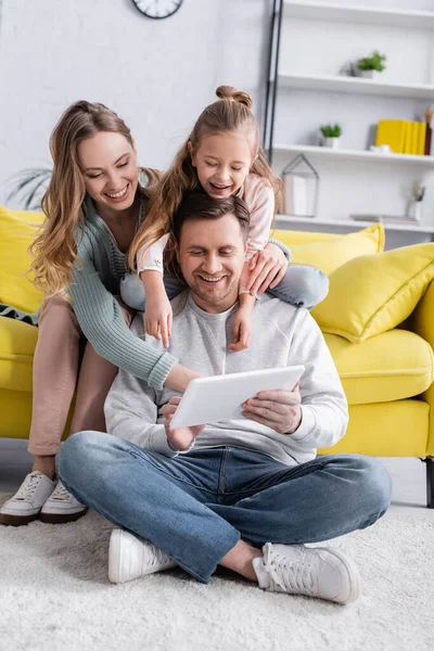 Man using digital tablet on floor near family on couch — Stock Photo