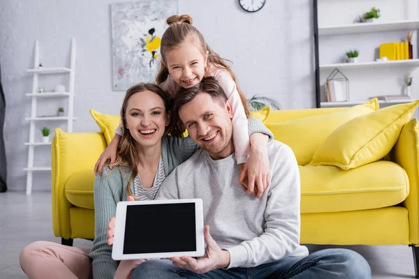 Familia positiva con hija sosteniendo tableta digital con pantalla en blanco en casa - foto de stock