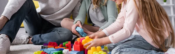 Vista ritagliata di bambino e madre che giocano mattoni vicino al padre, striscione — Foto stock