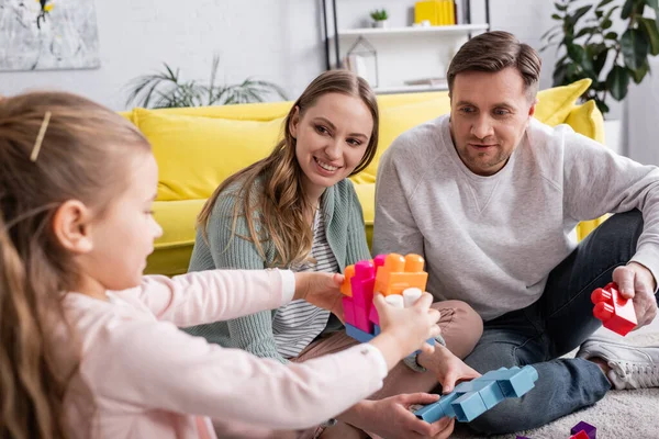 Padres positivos mirando a un niño jugando bloques de construcción en primer plano borroso - foto de stock