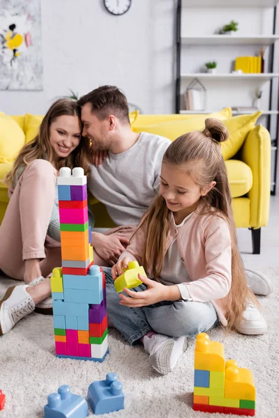 Niño sosteniendo bloque de construcción cerca de los padres en casa - foto de stock