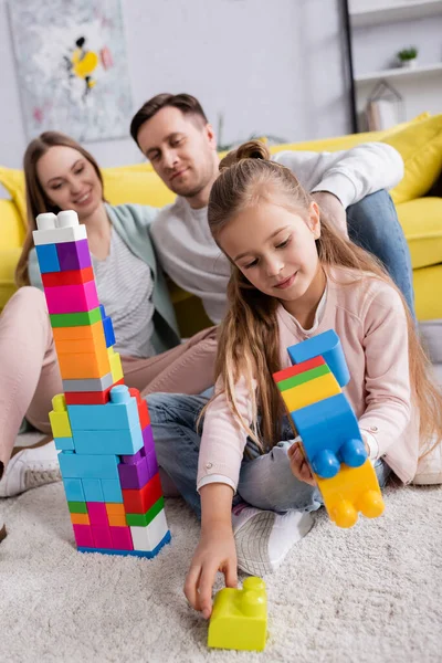 Kid apilar bloques de construcción cerca de los padres en la sala de estar - foto de stock