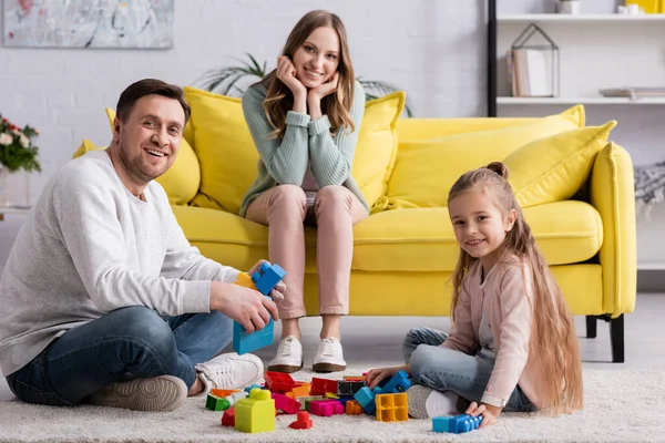 Lächelnde Familie blickt in die Kamera in der Nähe von Bauklötzen auf Teppich — Stockfoto