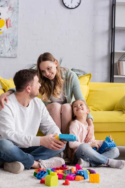 Mulher sorridente abraçando marido e filha com blocos de construção — Fotografia de Stock