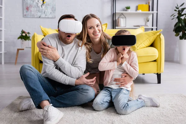 Woman hugging astonished husband and daughter in virtual reality headsets — Stock Photo