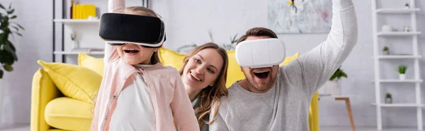 Pai alegre e filha usando fones de ouvido vr perto da mãe em casa, banner — Fotografia de Stock