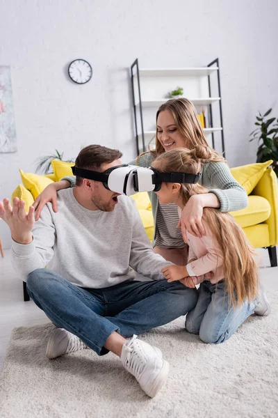 Father and daughter gaming in vr headsets near positive mother on carpet — Stock Photo