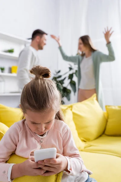 Niño usando smartphone mientras los padres discuten en casa - foto de stock