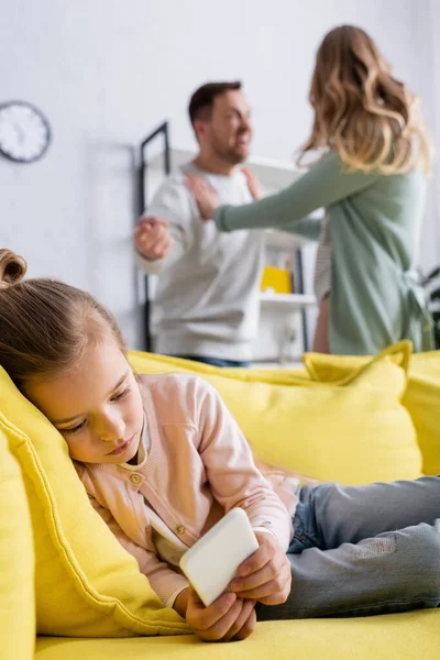 Mädchen benutzt Handy auf Couch in der Nähe von Eltern, die sich zu Hause streiten — Stockfoto