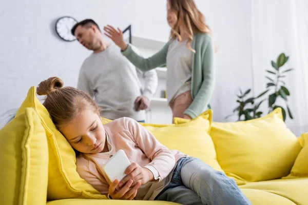 Kind benutzt Smartphone, während Mutter Vater auf verschwommenem Hintergrund ohrfeigt — Stockfoto