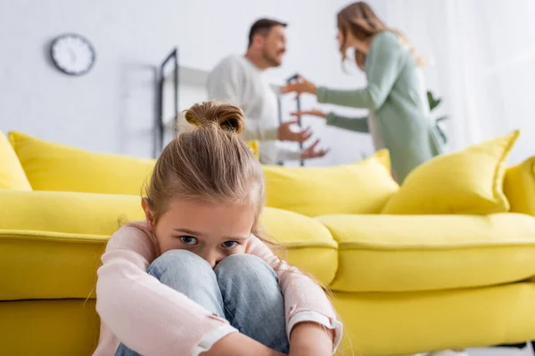 Chica asustada mirando a la cámara mientras los padres borrosos que tienen conflicto - foto de stock