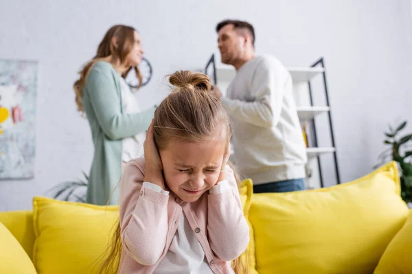 Chica cubriendo orejas cerca de padres peleando en casa - foto de stock