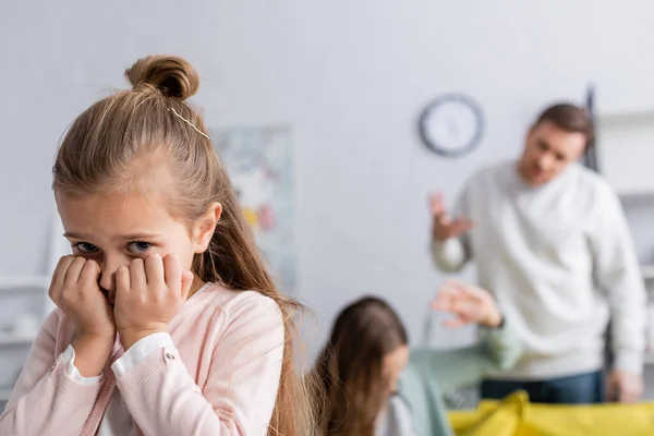 Enfant effrayé regardant la caméra près du père ayant un conflit avec la mère sur fond flou — Photo de stock