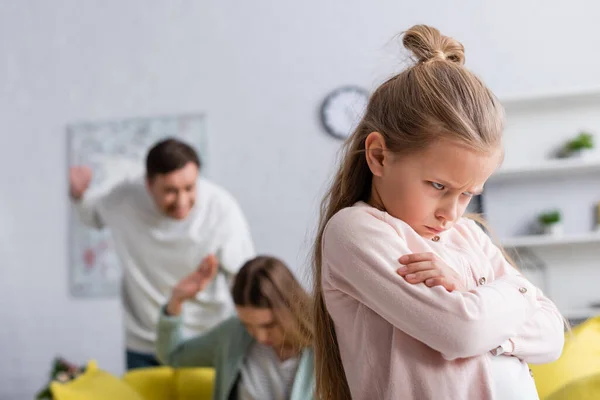 Angry kid standing near parents quarrelling on blurred background — Stock Photo