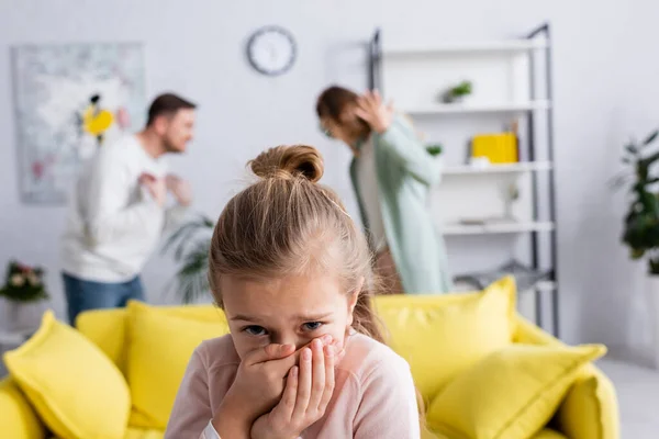 Bambino spaventato in piedi vicino ai genitori litigando in soggiorno su sfondo sfocato — Foto stock