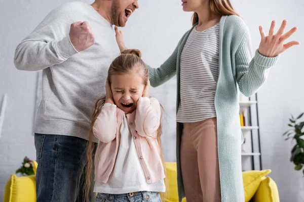 Frightened girl standing between parents quarreling — Stock Photo