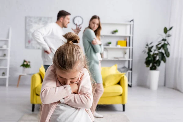 Niño disgustado con los brazos cruzados de pie cerca de padre peleando con la madre - foto de stock