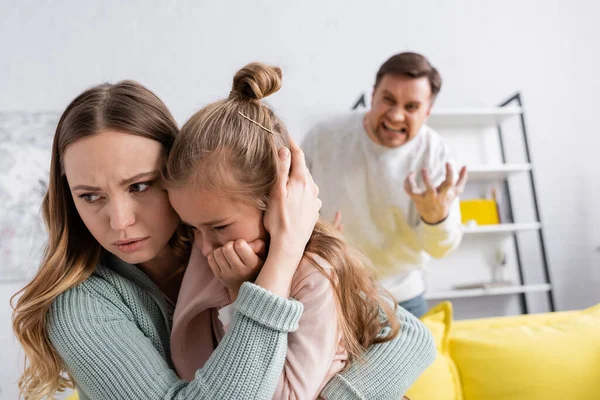 Woman hugging daughter while husband screaming on blurred background — Stock Photo