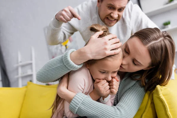 Mujer abrazando asustado niño cerca enojado marido en borrosa fondo - foto de stock