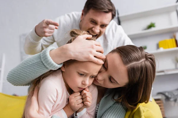 Woman covering frightened kid near irritated husband on blurred background — Stock Photo